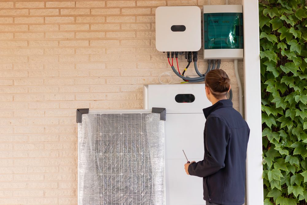 Technician checking a hybrid inverter and lithium battery installed on a brick wall