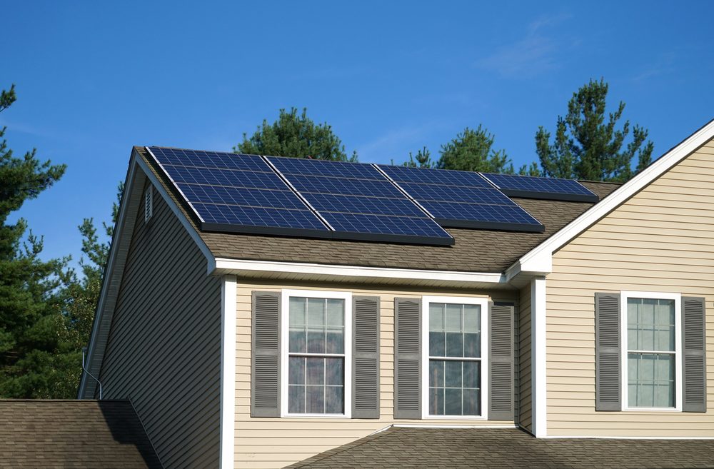 Rooftop solar panels on a house with a shingle roof under a clear blue sky